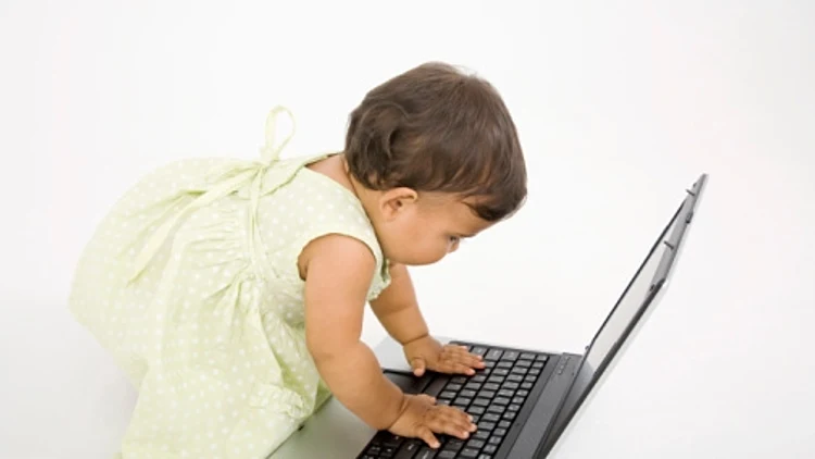 תינוקת כורעת מעל מחשב נייד