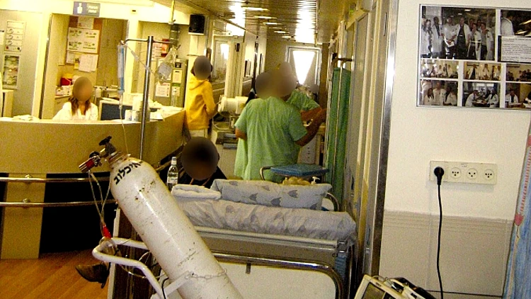 מיטה במסדרון במחלקה פנימית באיכילוב ובה חולה המסתייעת בבלון חמצן