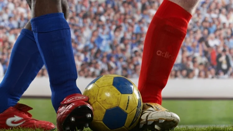 שתי רגליים של שני כדורגלנים, האחד עם גרב אדומה והשני עם גרב כחולה וכדור ביניהם, קהל מאחורה