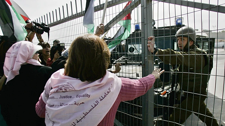 חייל ישראלי עוצר מפגינים פלסטינים מלפתוח את השער ביום האישה הבינלאומי במחסום קלנדיה סמוך לרמאללה