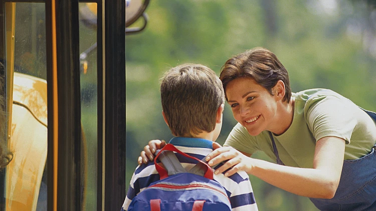 ילד עם ילקוט גב כחול נפרד מאמא שלו לפני העליה לאוטובוס לבית הספר