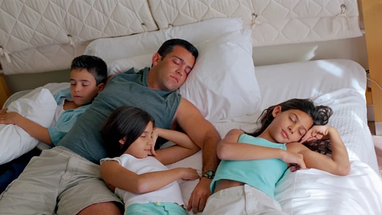 שלושה ילדים ואבא ישנים יחד במיטה במלון