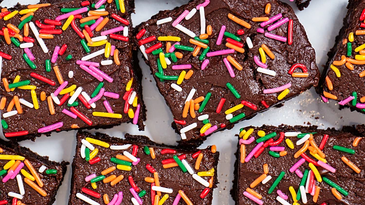Homemade,chocolate,frosted,brownies,with,rainbow,sprinkles,on,a,white