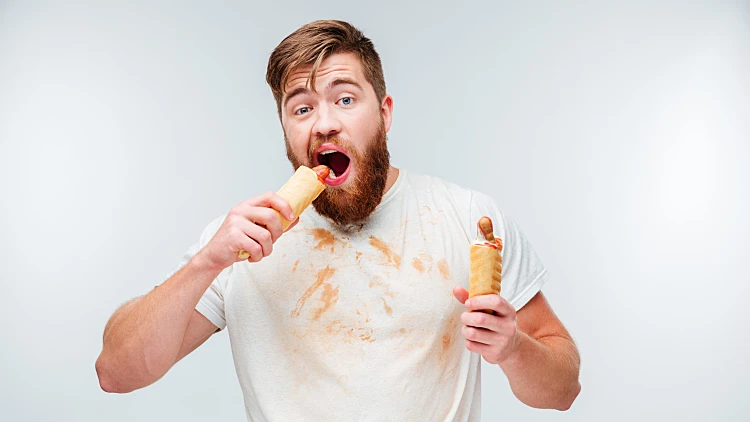 Hungry,bearded,man,in,dirty,shirt,biting,two,hotdogs,isolated