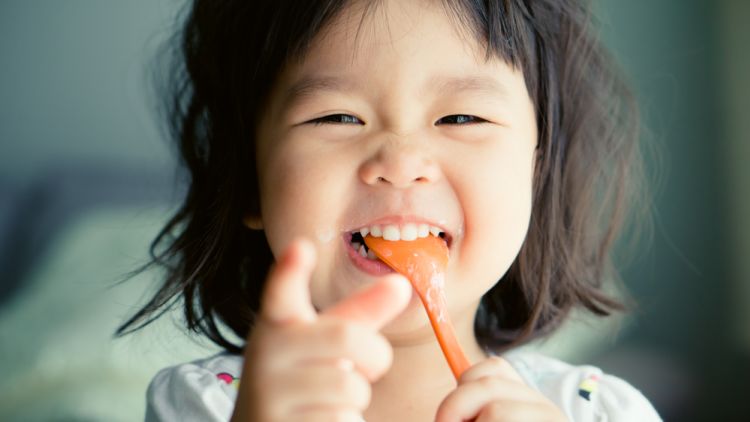 Happy,little,asian,child,girl,eating,yogurt,spoon,in,mouth.delicious,