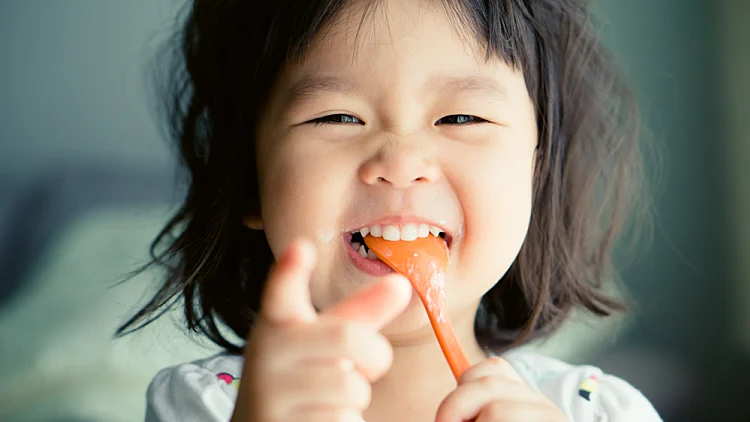Happy,little,asian,child,girl,eating,yogurt,spoon,in,mouth.delicious,