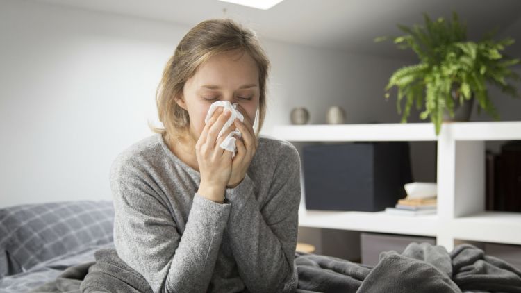 Sick Woman Sitting In Bed, Blowing Nose With Napkin