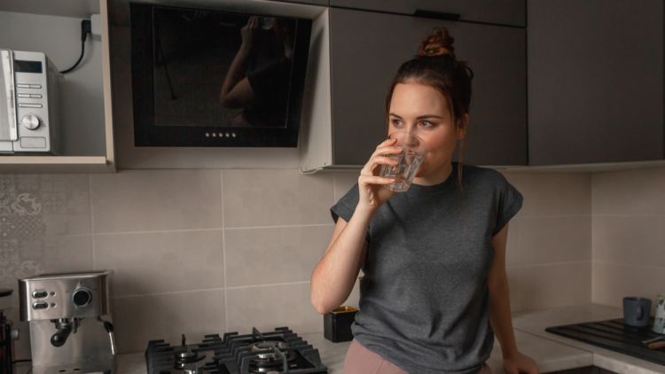 A,young,brunette,woman,stands,in,the,kitchen,and,drinks