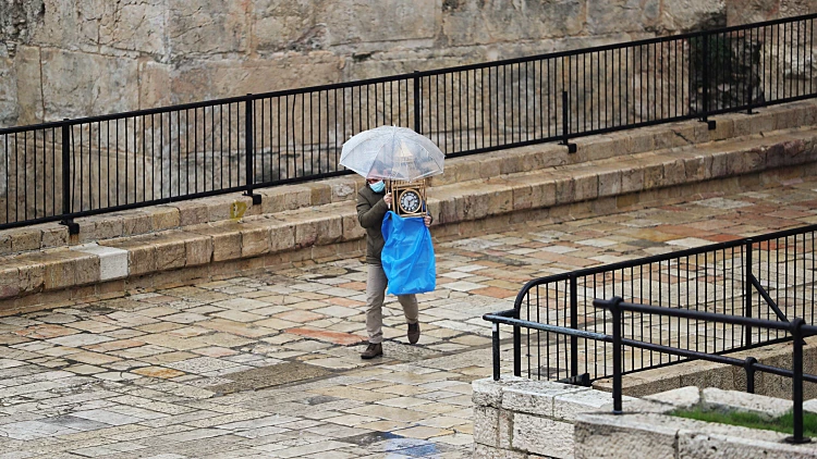 A Man Uses An Umbrella As He Carries A Clock While It Rains, Near Damascus Gate Just Outside Jerusalem's Old City