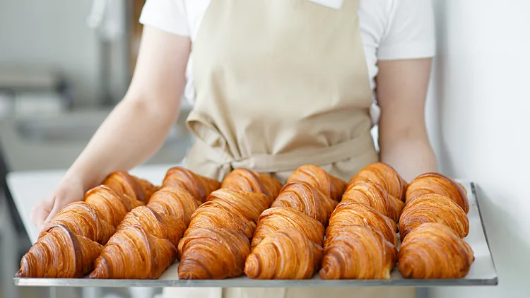 Baker,carrying,freshly,baked,crispy,golden,croissants,on,a,metal