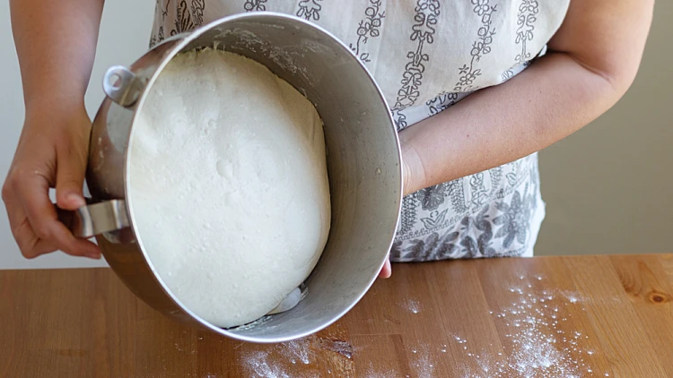 Female,hands,hold,a,metal,bowl,with,kneading,dough.,the
