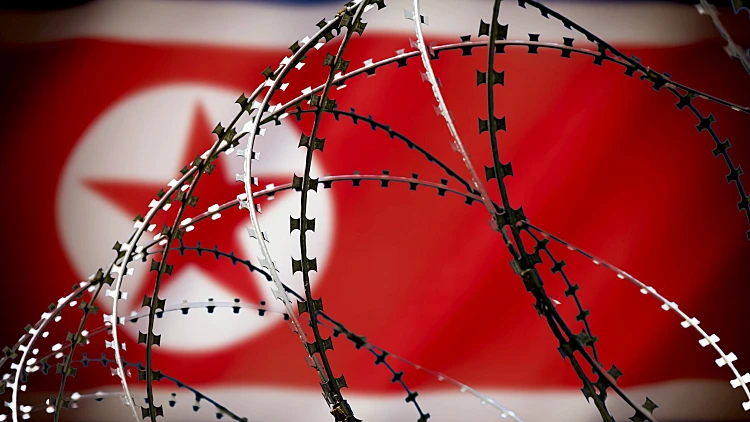 The,flag,of,north,korea,behind,barbed,wire.,concept:,aggressor