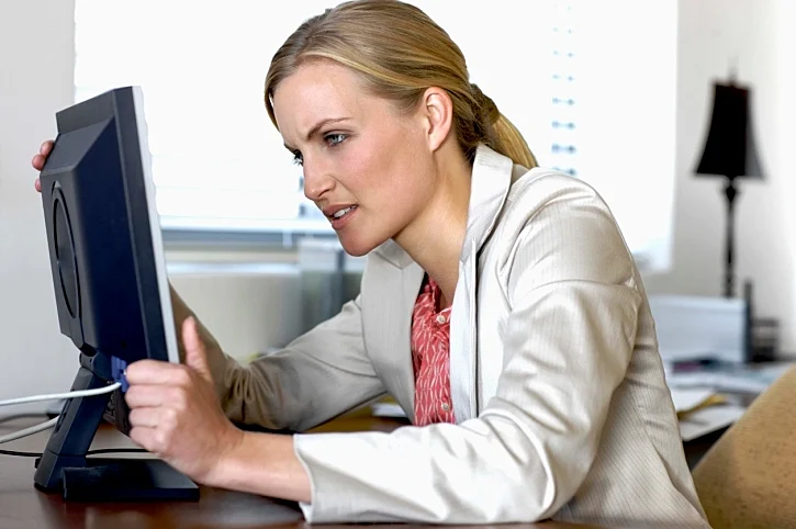 אשת עסקים מחזיקה במסך מחשב, מתוסכלת