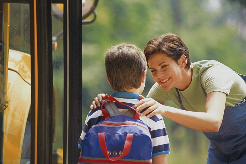 ילד עם ילקוט גב כחול נפרד מאמא שלו לפני העליה לאוטובוס לבית הספר