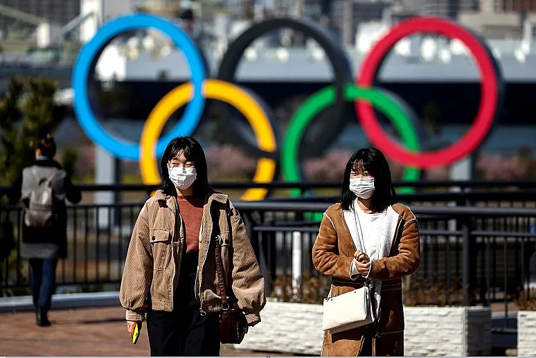 יפנים עוטים מסכות מפני קורונה מול סמל האולימפיאדה בטוקיו