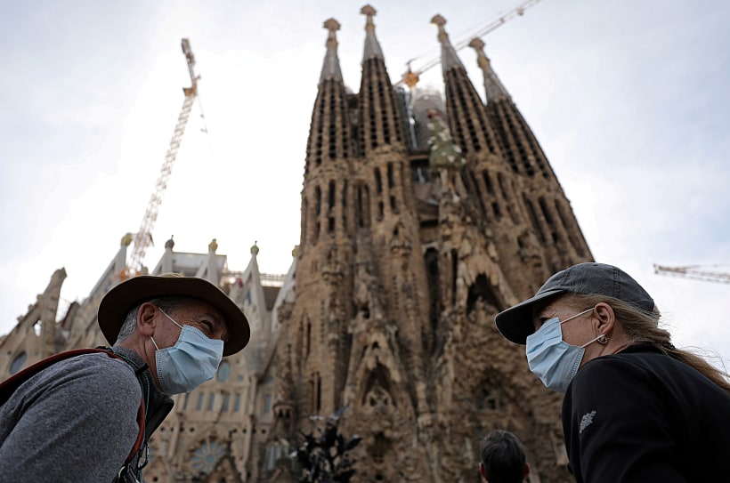 תיירים במסכות חולפים על פני קתדרלת הסגרדה פמיליה בברצלונה