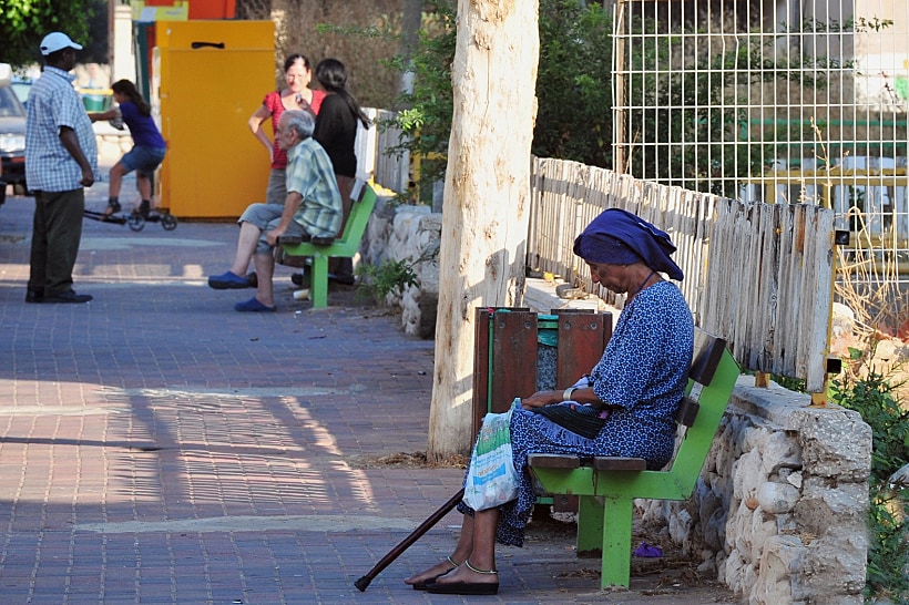אישה מבוגרת יושבת על ספסל בשכונת מצוקה