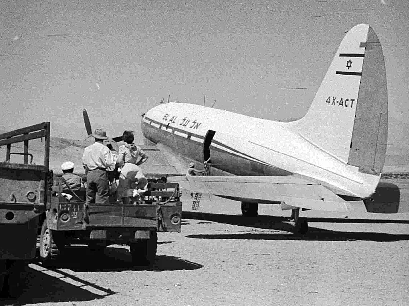 מטוס אל־על 4X-ACT ורכב צבאי (עם אזרחים) בנמל התעופה באילת (1952 לערך)