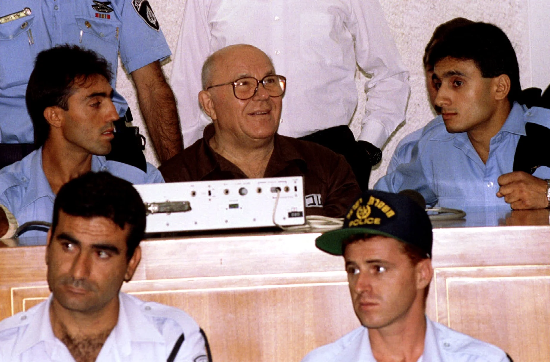 מוקף סוהרים ושוטרים ומחייך בעודו מחכה לקרוא את ההחלטה של יולי 29. דמיאניוק הורשע בשנת 1988 על היותו מפעיל תא הגזים במחנה הריכוז טרבלינקה במלחמת העולם השנייה