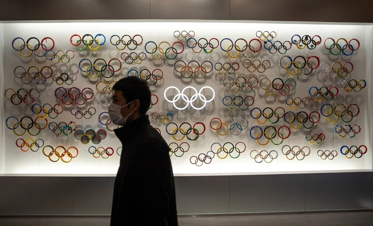 יפנים עוטים מסכות מפני קורונה מול סמל האולימפיאדה בטוקיו