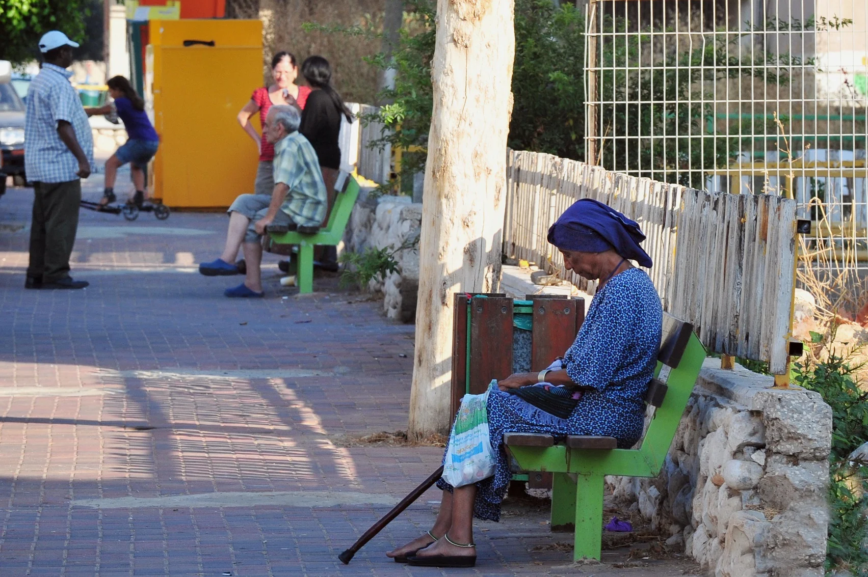 אישה מבוגרת יושבת על ספסל בשכונת מצוקה
