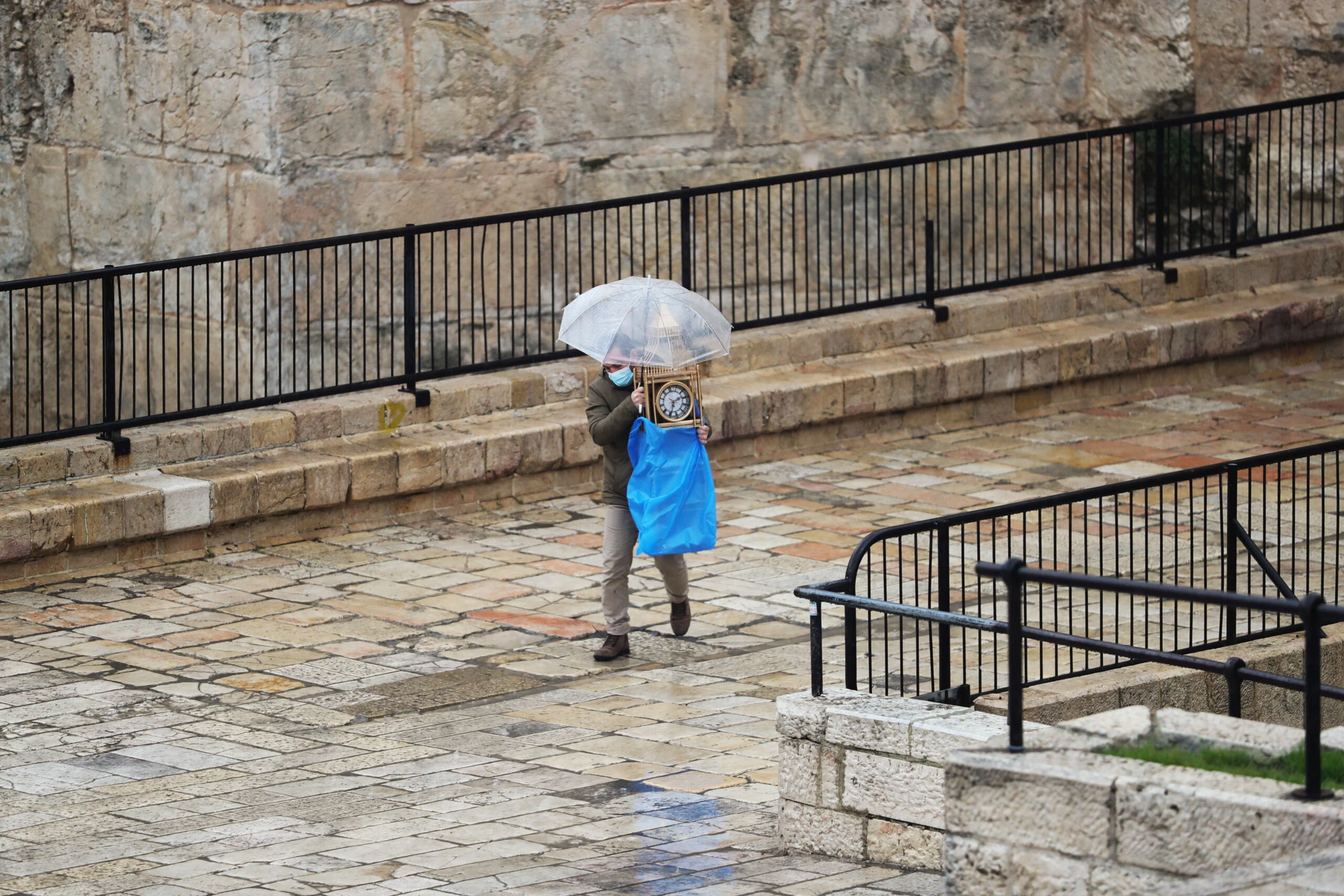A Man Uses An Umbrella As He Carries A Clock While It Rains, Near Damascus Gate Just Outside Jerusalem's Old City