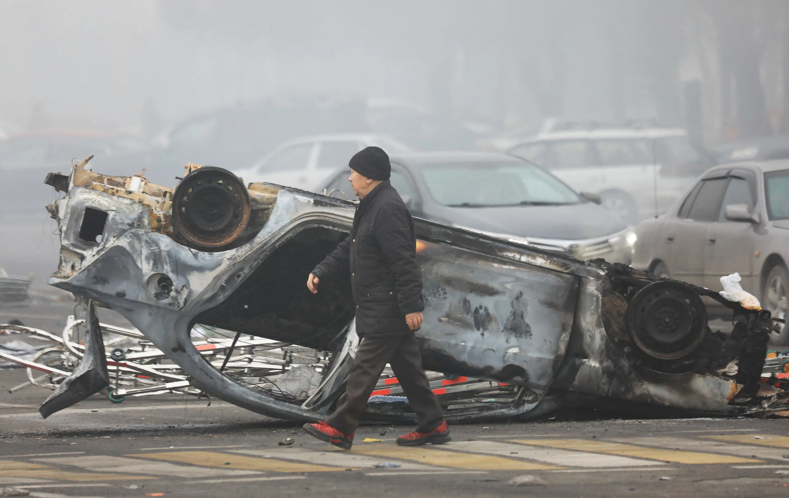 A Man Walks Past A Car That Was Burned During The Protests In Almaty
