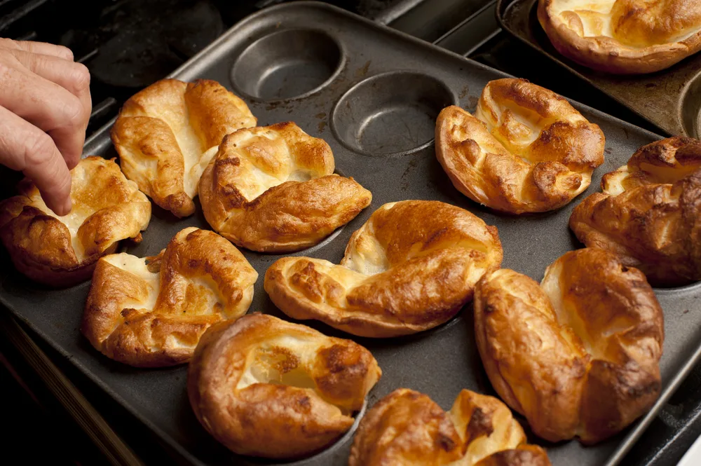 Man,removing,freshly,baked,individual,fluffy,golden,yorkshire,puddings,from