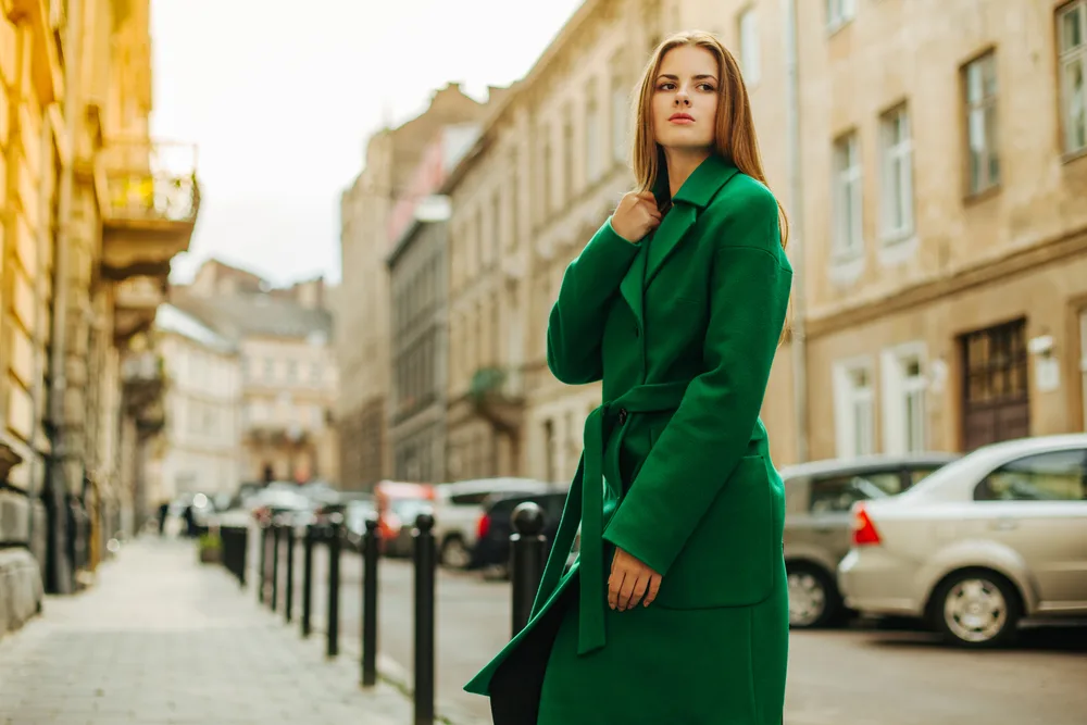 Young,beautiful,woman,in,a,dark,green,coat,against,a